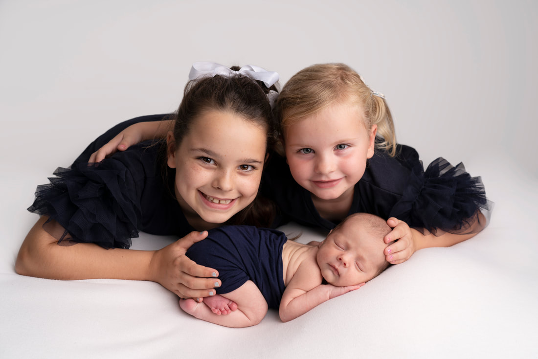 Big sister's proudly show their new baby brother in photography studio Bexley
